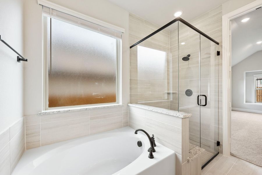 Master bathroom with soaking tub, glass-enclosed shower, and light tile walls next to a frosted window Master bathroom with soaking tub, glass-enclosed shower, and light tile walls next to a frosted window