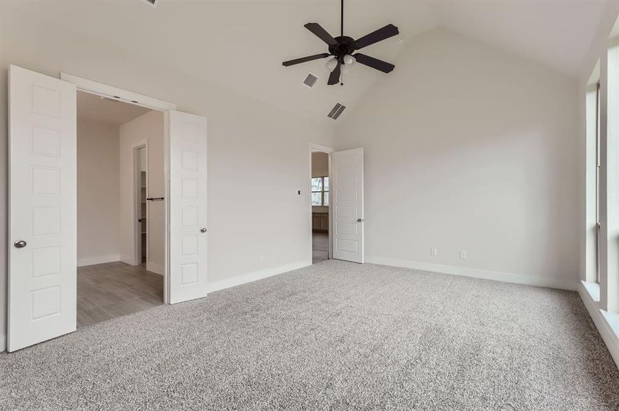 Unfurnished bedroom with ceiling fan, light colored carpet, and high vaulted ceiling