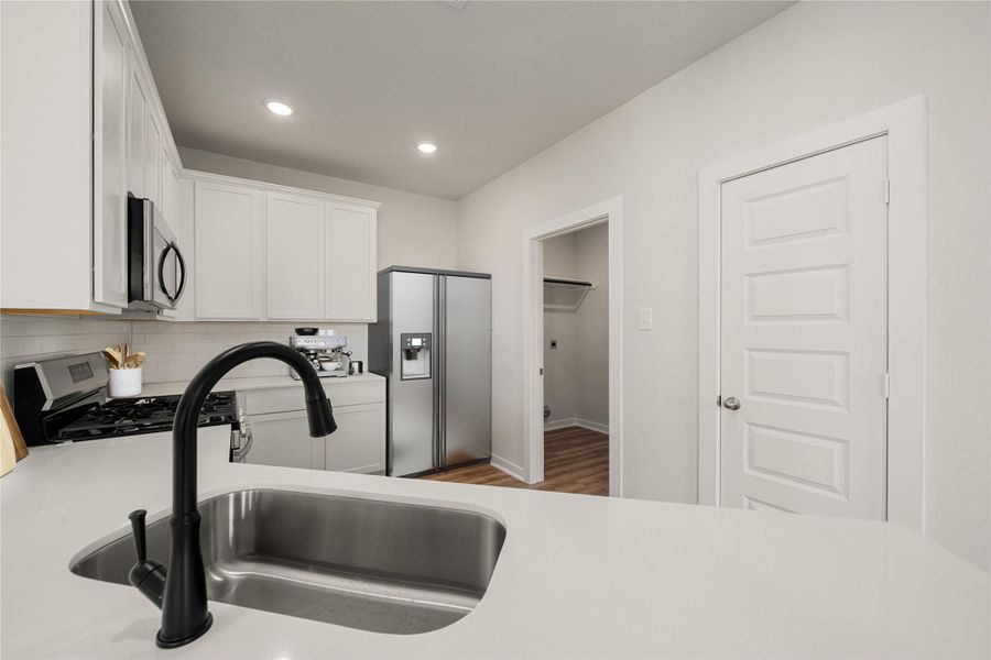 The kitchen features crisp white cabinetry, sleek countertops, and stainless steel appliances that complement the clean design. The open layout allows for easy flow into adjoining spaces, while recessed lighting and a stylish black faucet add a touch of sophistication. A walk-in pantry offers ample storage, combining functionality with contemporary charm. The kitchen features crisp white cabinetry, sleek countertops, and stainless steel appliances that complement the clean design. The open layout allows for easy flow into adjoining spaces, while recessed lighting and a stylish black faucet add a touch of sophistication. A walk-in pantry offers ample storage, combining functionality with contemporary charm.