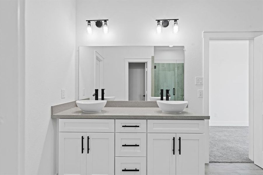 Modern bathroom with dual vessel sinks, sleek cabinetry, and recessed lighting. Bright and clean design.