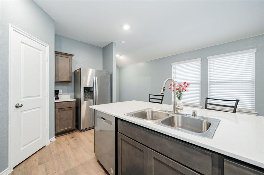 Kitchen with dark brown cabinets, appliances with stainless steel finishes, light countertops, light wood-style flooring, and recessed lighting Kitchen with dark brown cabinets, appliances with stainless steel finishes, light countertops, light wood-style flooring, and recessed lighting