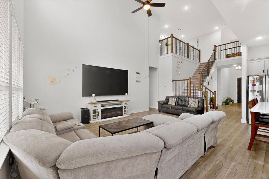 Living area with light wood-style floors, ceiling fan, stairs, a high ceiling, and a glass covered fireplace