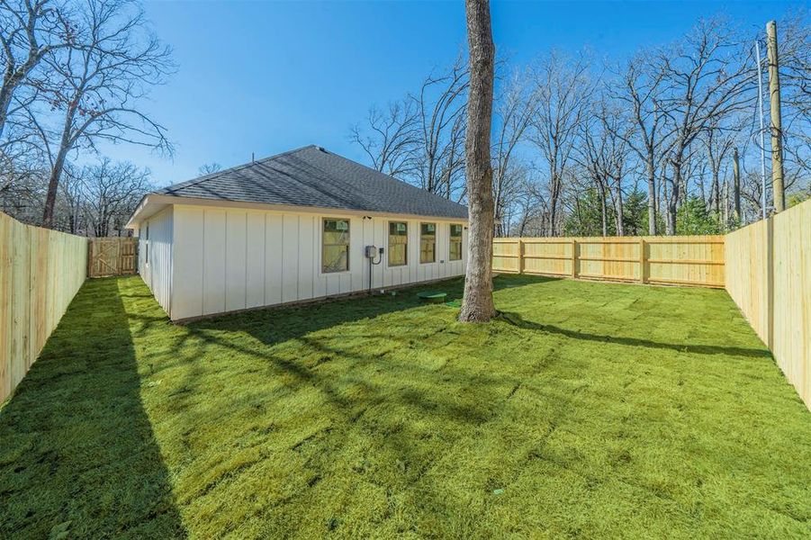 Rear view of property featuring a yard, a shingled roof, and a fenced backyard