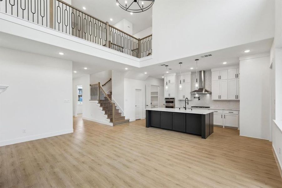 Kitchen with a kitchen island with sink, hanging light fixtures, white cabinets, wall chimney exhaust hood, and light wood-type flooring