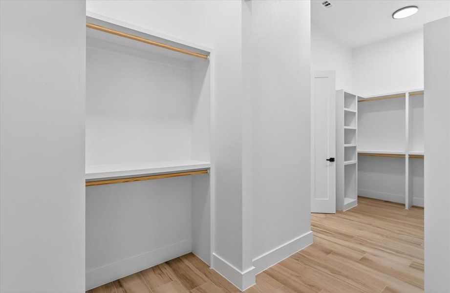 Spacious closet featuring built-in shelving, hanging rods, light wood-finish flooring, and white trim