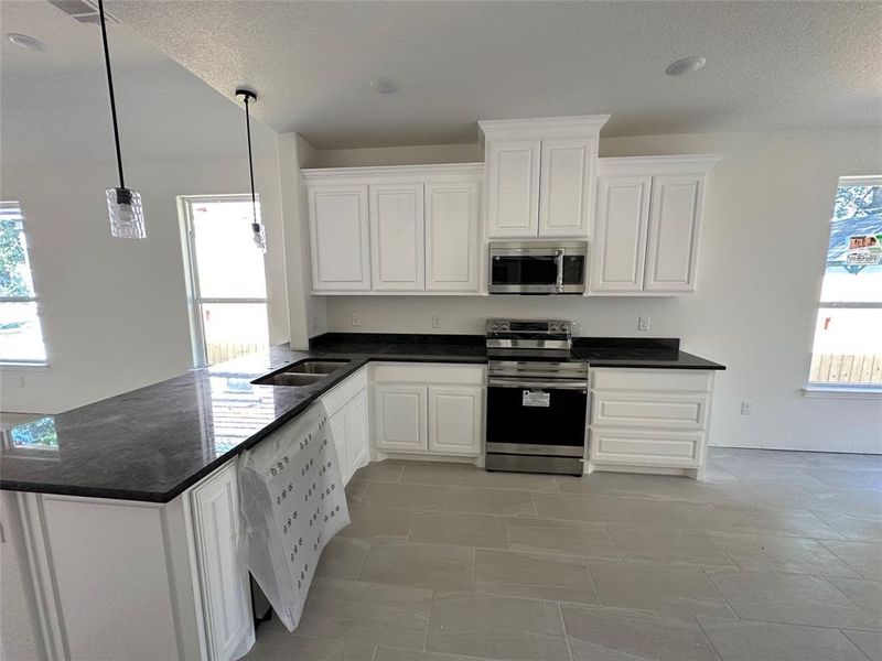 Kitchen featuring white cabinetry, stainless steel appliances, plenty of natural light, and hanging light fixtures