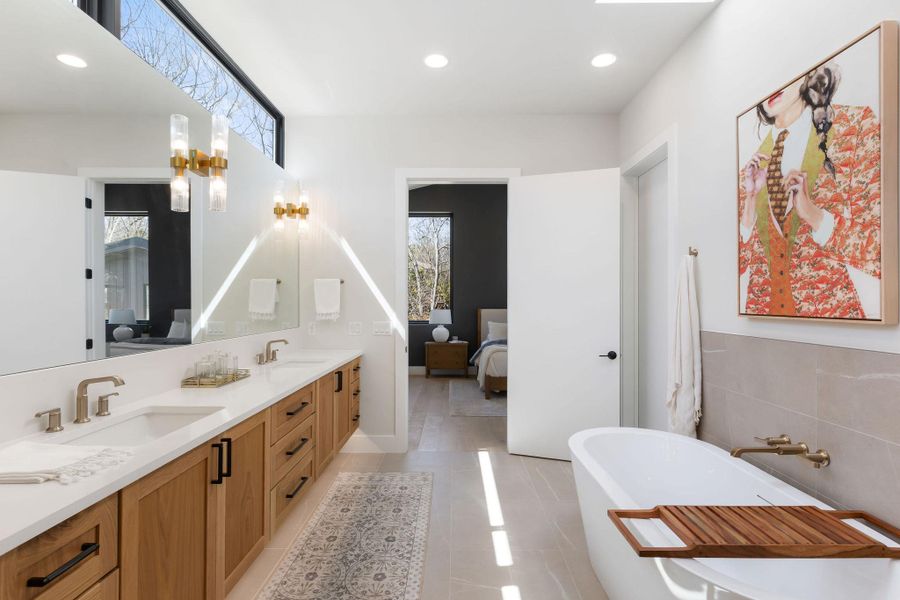 Ensuite bathroom featuring double vanity, connected bathroom, a freestanding bath, and a sink