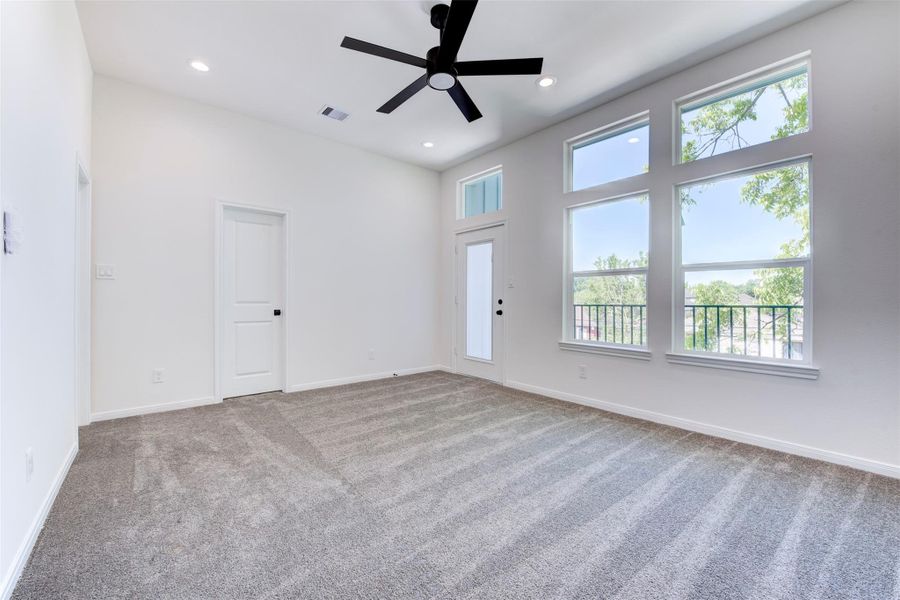 Spacious primary suite featuring plush carpet, a ceiling fan with light kit, and recessed lighting throughout. Abundant natural light pours in through large windows, while direct access to a private balcony adds a peaceful, elevated retreat.