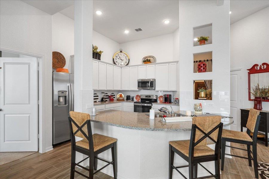Kitchen with stainless steel appliances, a high ceiling, white cabinets, tasteful backsplash, and light stone countertops Kitchen with stainless steel appliances, a high ceiling, white cabinets, tasteful backsplash, and light stone countertops