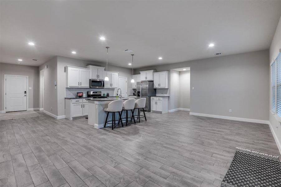 Kitchen with white cabinets, a center island with sink, decorative light fixtures, and a breakfast bar area