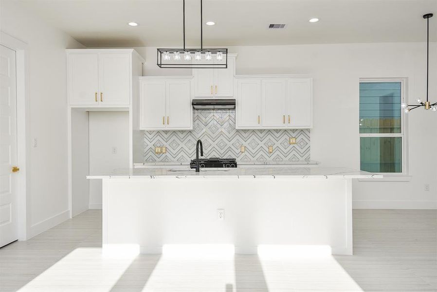 A chef’s dream! This well-lit open kitchen is perfect for entertaining, featuring a spacious quartz island with breakfast bar seating, sleek stainless steel appliances, and elegant gold hardware. The stunning backsplash adds a touch of luxury to this modern culinary space.