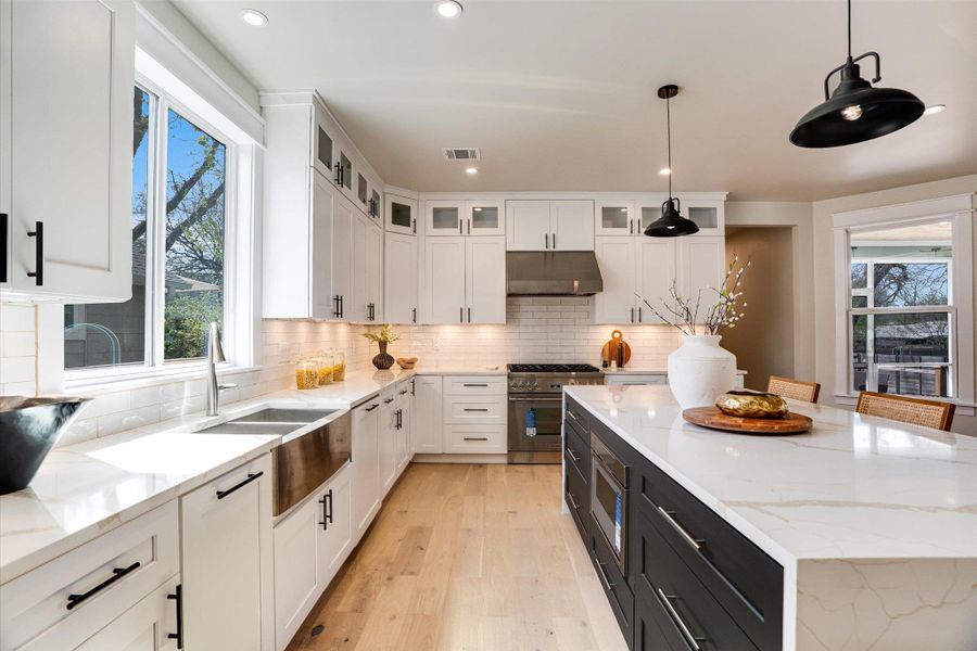 Well-appointed kitchen featuring white cabinetry, a stainless steel farmhouse sink, a large island with a waterfall countertop, and hardwood flooring Well-appointed kitchen featuring white cabinetry, a stainless steel farmhouse sink, a large island with a waterfall countertop, and hardwood flooring