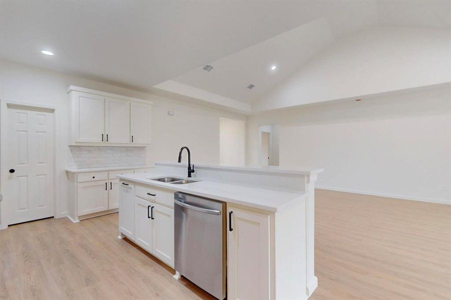 Kitchen featuring light wood finished floors, a sink, dishwasher, white cabinetry, and a kitchen island with sink