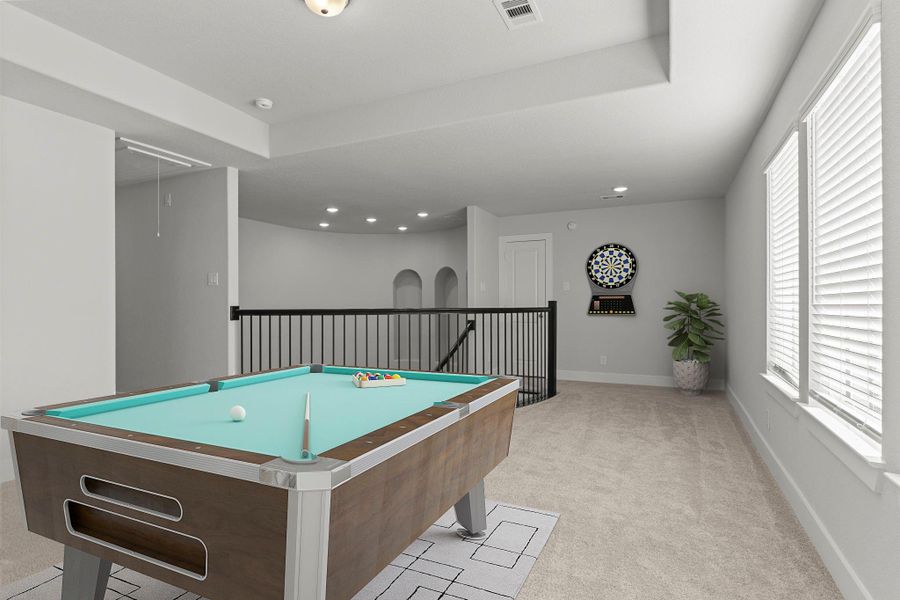 Another view of the game room showcases the elegant iron railing overlooking the staircase and foyer below. Natural light pours in through the windows, creating a warm and inviting space for gatherings. *Photo Staged*