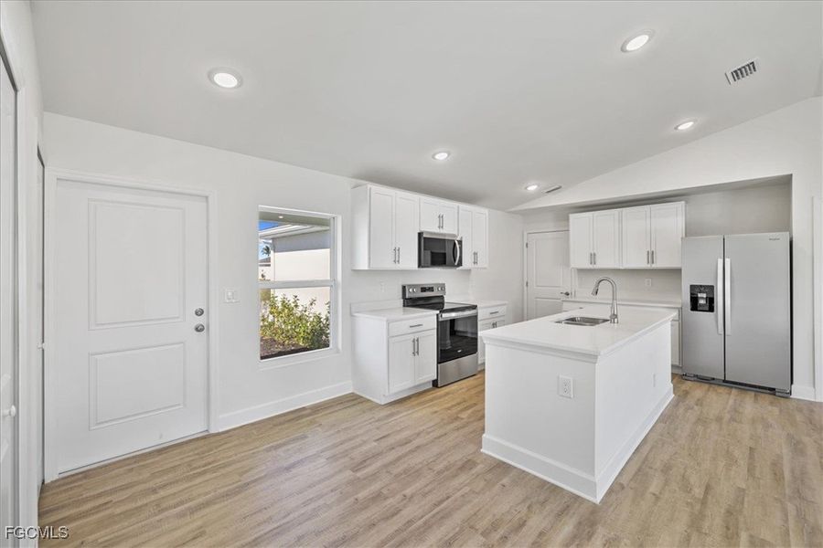 Kitchen featuring stainless steel appliances, white cabinets, a center island with sink, light wood-style flooring, and lofted ceiling