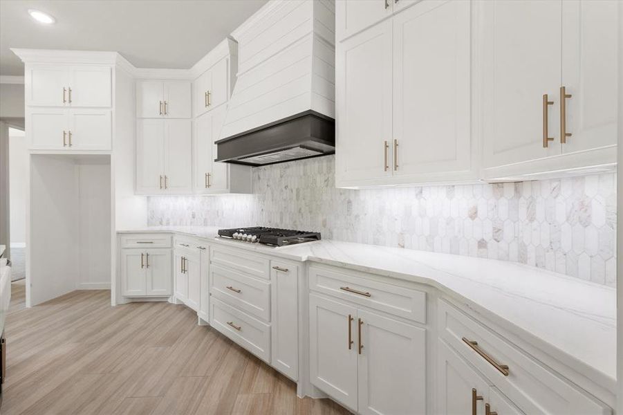 Modern kitchen featuring white cabinetry with gold-finish hardware, a gas cooktop, and a white pick-tile backsplash