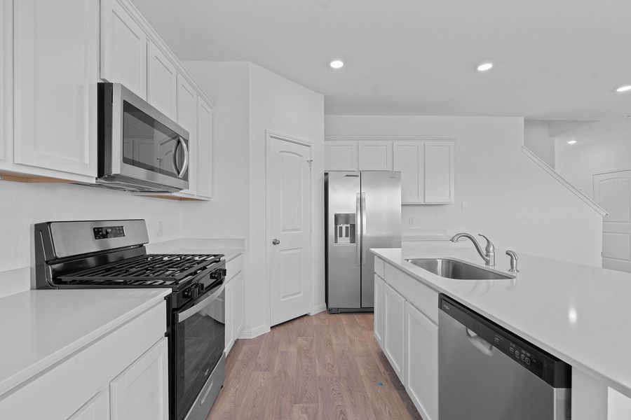 Kitchen with appliances with stainless steel finishes, light wood-type flooring, white cabinetry, recessed lighting, and light stone counters Kitchen with appliances with stainless steel finishes, light wood-type flooring, white cabinetry, recessed lighting, and light stone counters