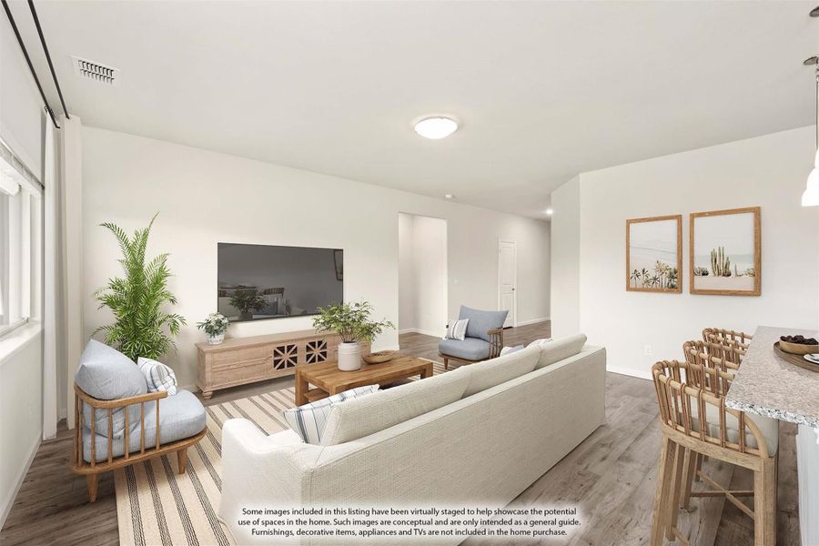 Open living room with light wood floors, white sofa, TV console, and adjacent dining area with bar seating