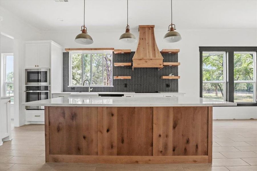 Kitchen featuring decorative light fixtures, open shelves, stainless steel appliances, light stone counters, and a kitchen island