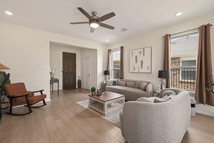 Bright living room with upgraded light wood floors, recessed lighting, ceiling fan, and large windows.