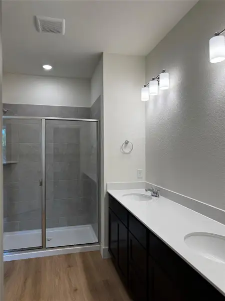 Full bathroom featuring a textured wall, a stall shower, wood finished floors, double vanity, and a textured ceiling Full bathroom featuring a textured wall, a stall shower, wood finished floors, double vanity, and a textured ceiling