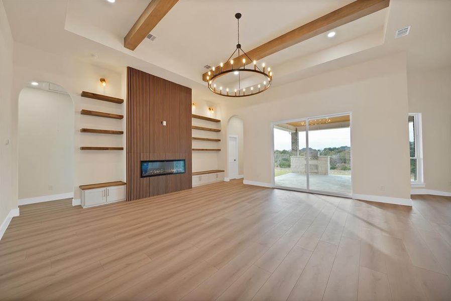 Unfurnished living room featuring arched walkways, beamed ceiling, light wood-type flooring, a fireplace, and a towering ceiling Unfurnished living room featuring arched walkways, beamed ceiling, light wood-type flooring, a fireplace, and a towering ceiling