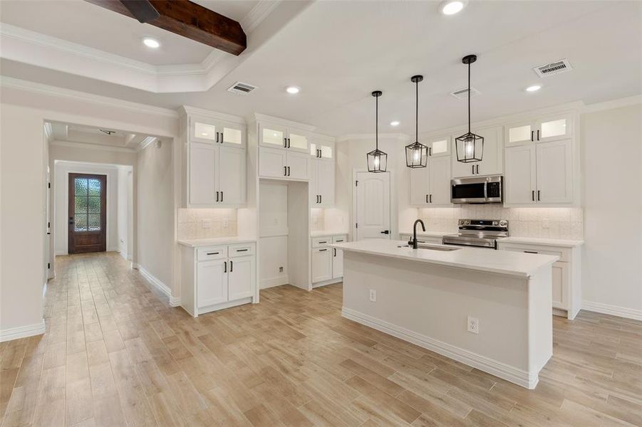 Kitchen featuring light wood-type flooring, crown molding, stainless steel appliances, an island with sink, and white cabinets