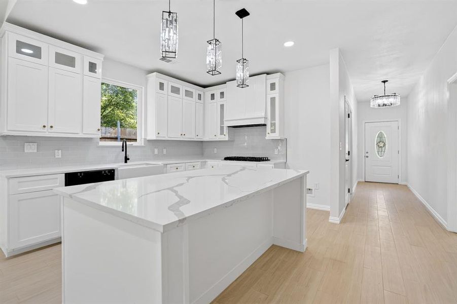 Contemporary kitchen featuring an oversized island with a quartz-finish countertop, white cabinetry with gold-tone hardware, a white farmhouse sink with a black faucet, and three pendant light fixtures