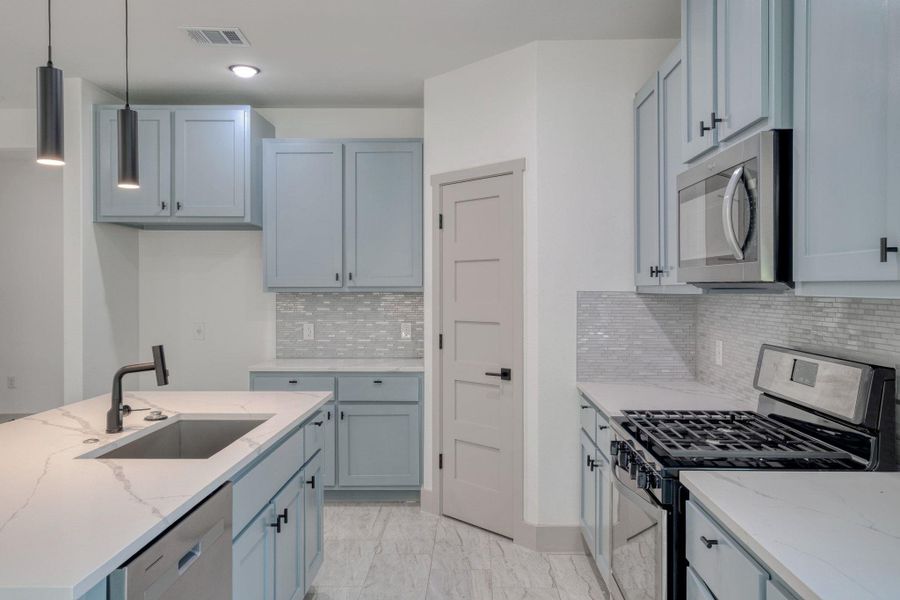 Kitchen with stainless steel appliances, hanging light fixtures, light stone countertops, an island with sink, and recessed lighting Kitchen with stainless steel appliances, hanging light fixtures, light stone countertops, an island with sink, and recessed lighting
