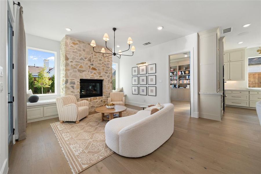 Living room with a stone fireplace, light hardwood / wood-style floors, and an inviting chandelier