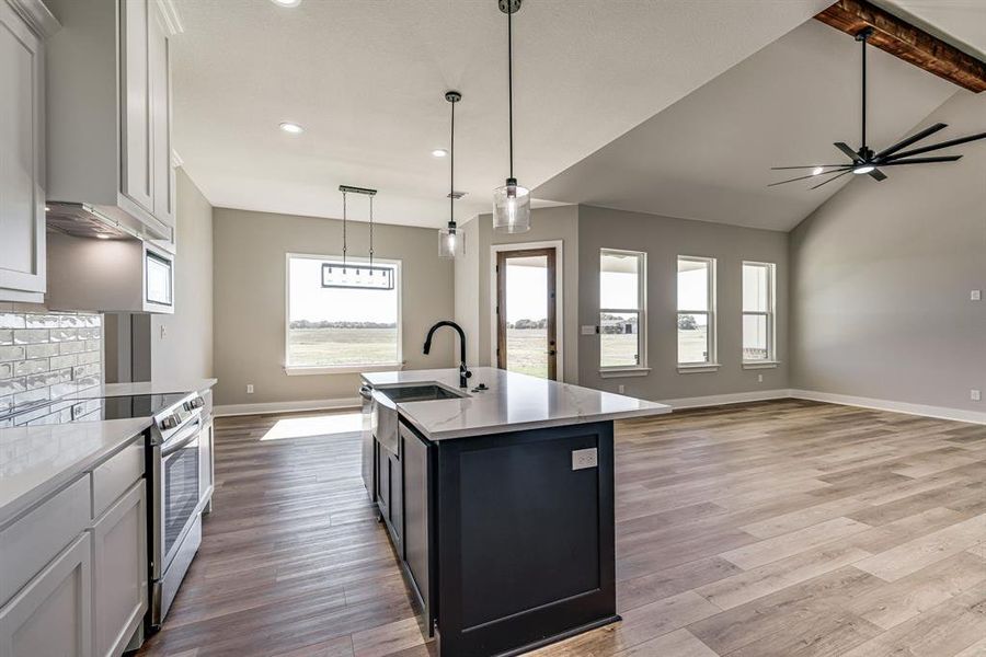 Kitchen featuring decorative light fixtures, a center island with sink, light wood-type flooring, and white cabinetry