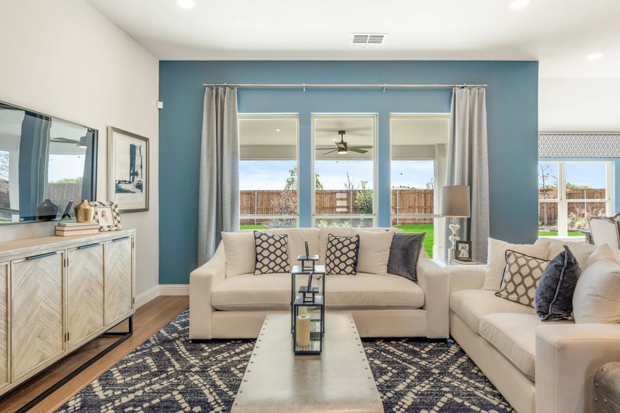 Living room with blue accent wall, cream sofas, patterned rug, and large windows overlooking backyard
