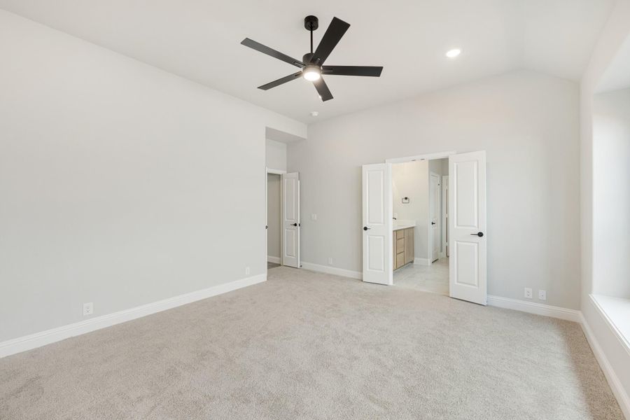 Empty bedroom with carpet, black ceiling fan, and open doors leading to bathroom and hallway