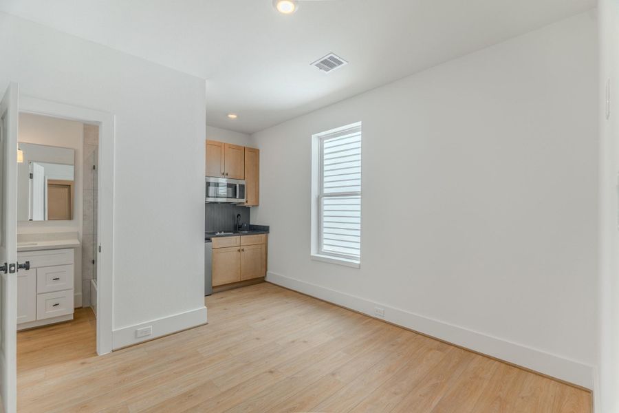 This photo shows a bright, compact room with light wood flooring and white walls. It features a small kitchenette with wooden cabinets and stainless steel appliances. A door leads to a bathroom with a white vanity. Ideal for a minimalist living space or studio apartment.Photo Disclaimer: Photos are representative of the community and may depict a similar floor plan, model home, or previously completed residence. This photo shows a bright, compact room with light wood flooring and white walls. It features a small kitchenette with wooden cabinets and stainless steel appliances. A door leads to a bathroom with a white vanity. Ideal for a minimalist living space or studio apartment.Photo Disclaimer: Photos are representative of the community and may depict a similar floor plan, model home, or previously completed residence.