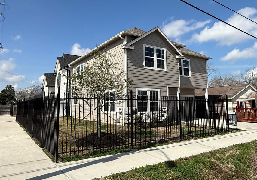 This is a modern two-story home with a light-colored exterior, large windows, and a fenced yard. It features a paved walkway and driveway, offering a clean and inviting curb appeal.