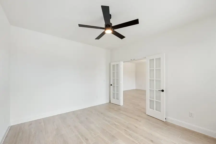 Empty room with light wood floors, black ceiling fan, and white French doors leading to adjacent room