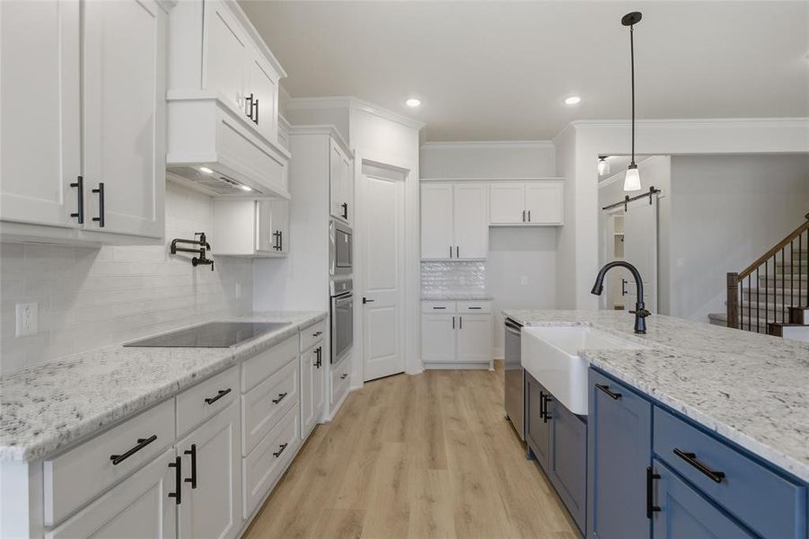 Two tone kitchen featuring dual tone cabinets, light stone countertops, light wood-type flooring, decorative light fixtures, and stainless steel appliances
