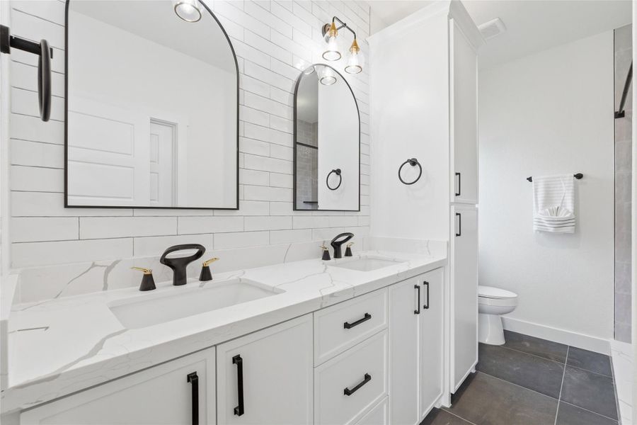 Modern en suite with stand-up shower, dual sinks and neutral finishes throughout, as well as a linen closet for additional storage.