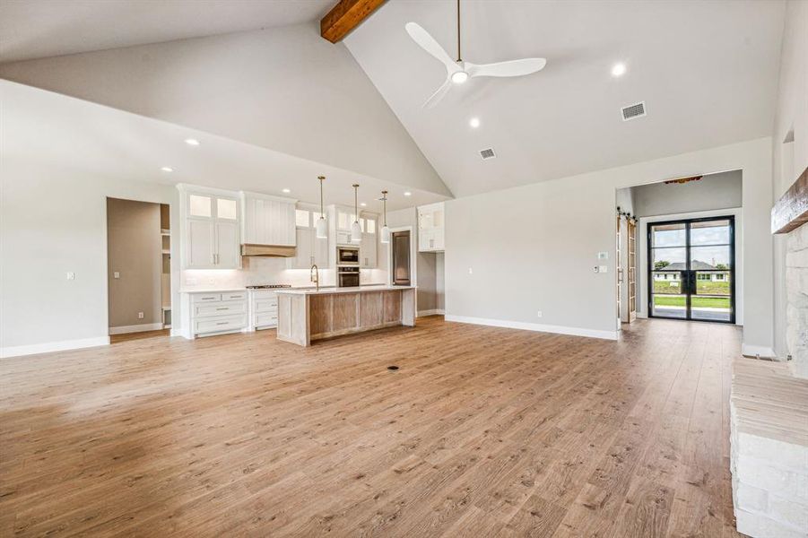 Unfurnished living room with ceiling fan, beamed ceiling, light hardwood / wood-style flooring, and high vaulted ceiling