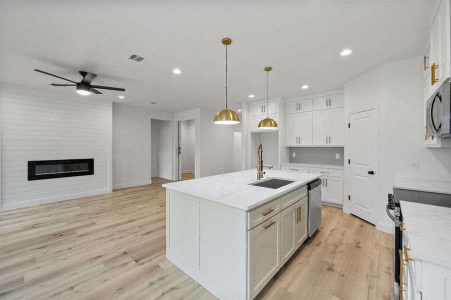 Kitchen with a large fireplace, a sink, visible vents, white cabinetry, and appliances with stainless steel finishes