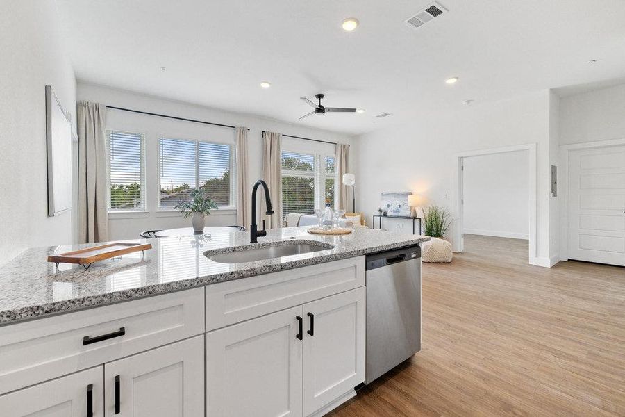 Kitchen with light stone countertops, white cabinets, light wood-style flooring, ceiling fan, and stainless steel dishwasher