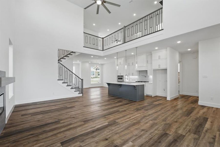 Unfurnished living room with stairs, baseboards, dark wood-style flooring, and ceiling fan with notable chandelier