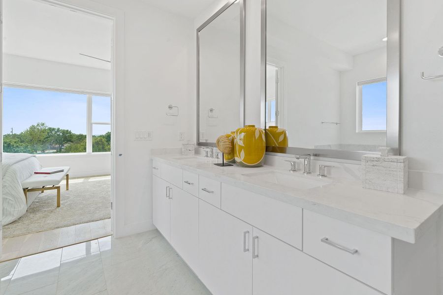 Bathroom with double vanity, healthy amount of natural light, light marble finish flooring, and connected bathroom