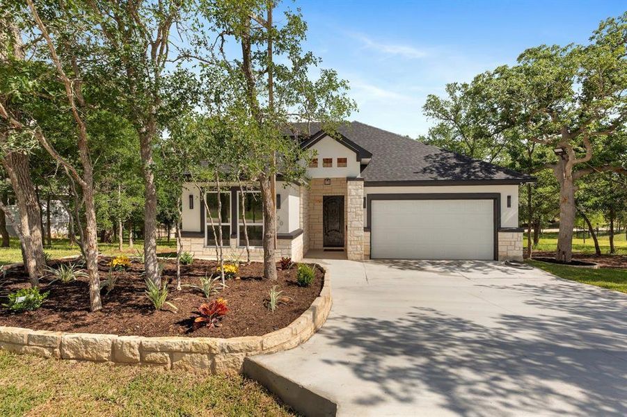 View of front facade featuring stone siding, an attached garage, concrete driveway, and a shingled roof