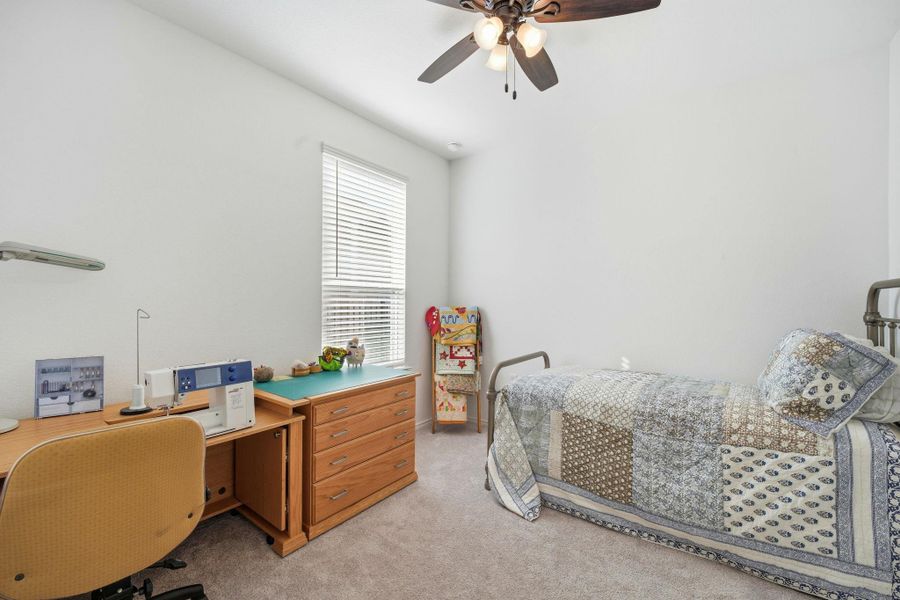 Bedroom with light colored carpet, a ceiling fan, and a desk