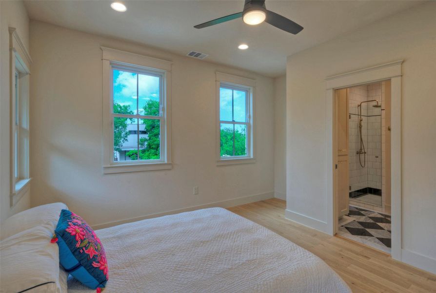 The well-lit primary bedroom features hardwood floors and an adjacent bathroom with exquisite tile.