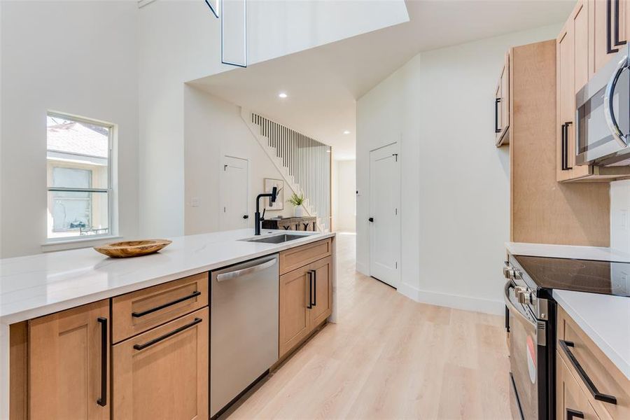 Kitchen featuring light wood-style flooring, stainless steel appliances, light stone countertops, and light wood finish cabinets