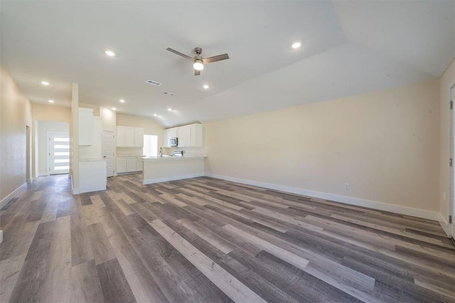 Unfurnished living room with baseboards, visible vents, a ceiling fan, wood finished floors, and vaulted ceiling