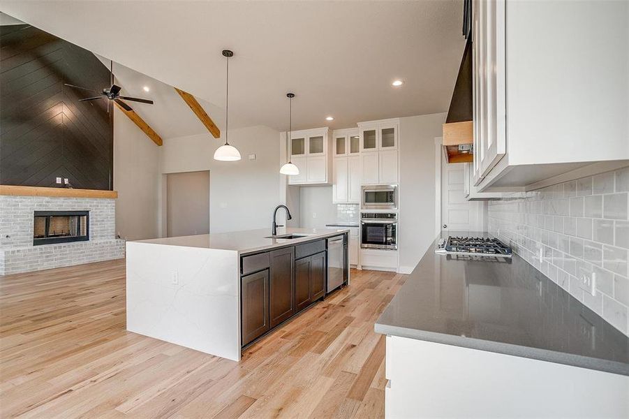 Kitchen featuring appliances with stainless steel finishes, sink, a fireplace, decorative backsplash, and a kitchen island with sink