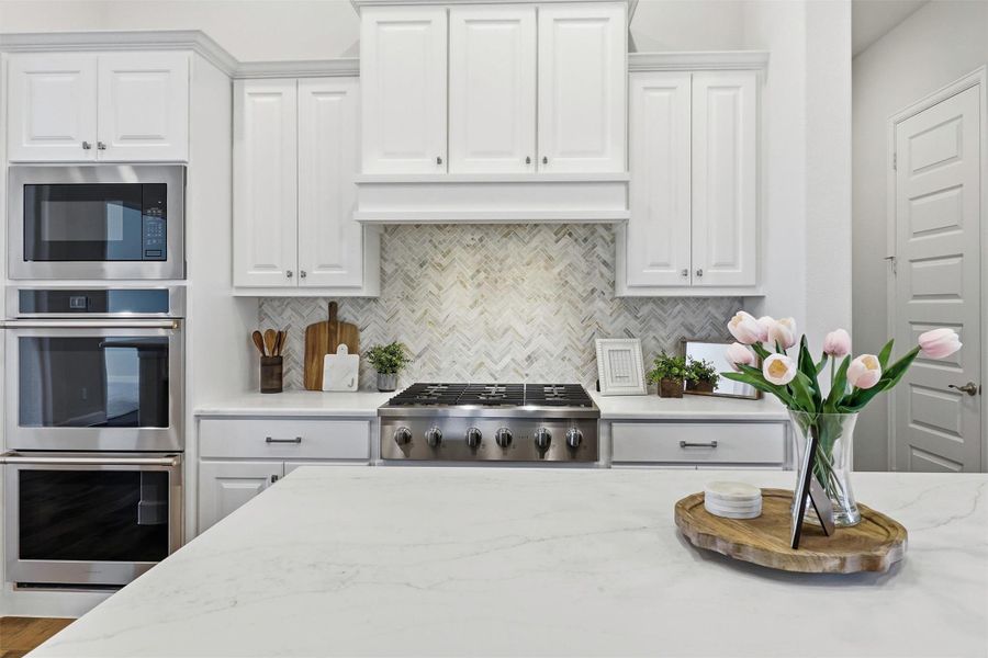 Imagine starting your mornings here. The herringbone marble backsplash catches the light just right, Calacatta Gold quartz countertops anchor the oversized island, and Monogram stainless appliances make cooking feel like a gift. Crisp white raised-panel cabinetry offers abundant storage while keeping the space bright and timeless.